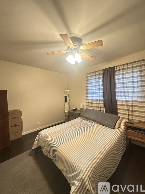 A bedroom with a bed, a ceiling fan, and a window with curtains.