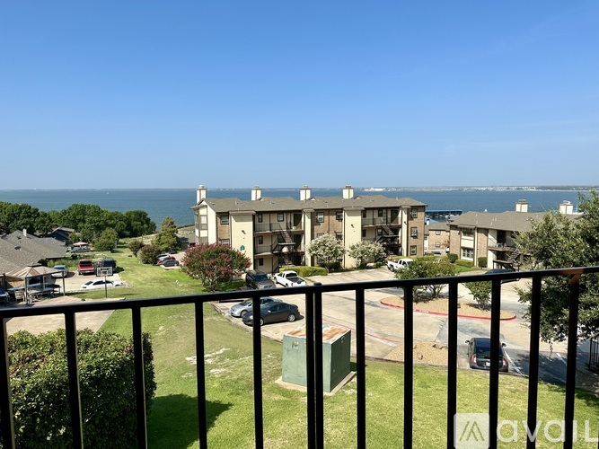 A balcony overlooks a grassy area with a building and a body of water in the distance.