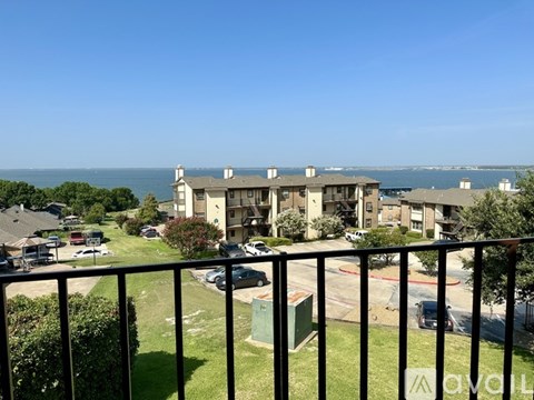 A balcony overlooks a grassy area with a building and a body of water in the distance.