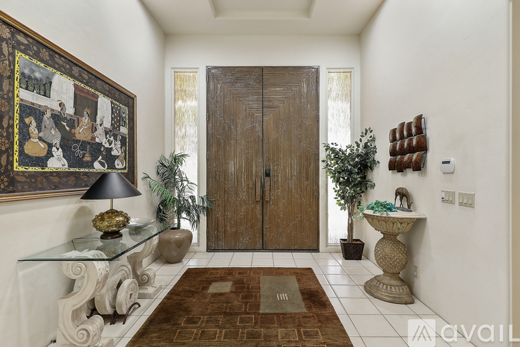 A hallway with a brown rug, a glass table, a lamp, and a framed picture on the wall.