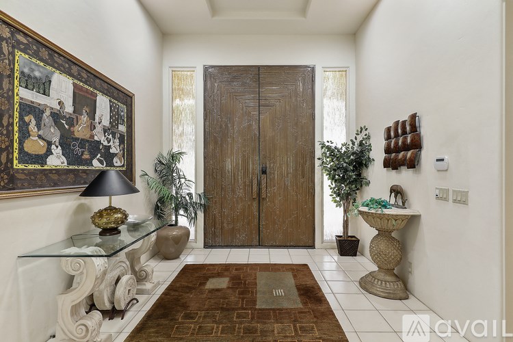 A hallway with a brown rug, a glass table, a lamp, and a framed picture on the wall.