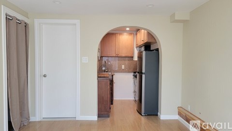 A kitchen with a refrigerator, sink, and cabinets under an archway.