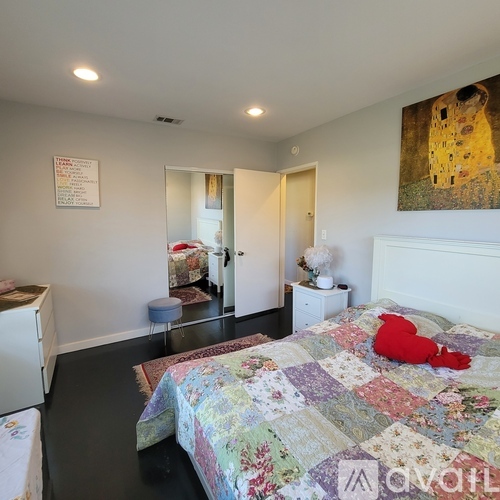 A bedroom with a bed, a washing machine, and a painting on the wall.