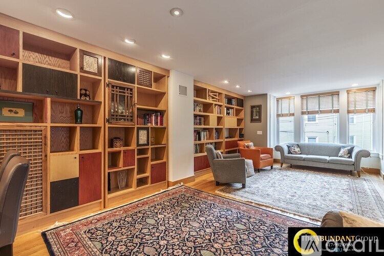 A living room with a large rug and a bookshelf filled with books.