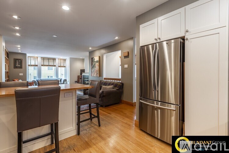 A modern kitchen with a stainless steel refrigerator and wooden flooring.