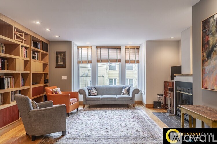 A living room with a grey couch, a wooden bookshelf, and a painting on the wall.