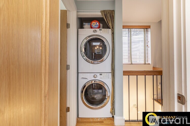 A white washing machine is in a small room with a wooden door.