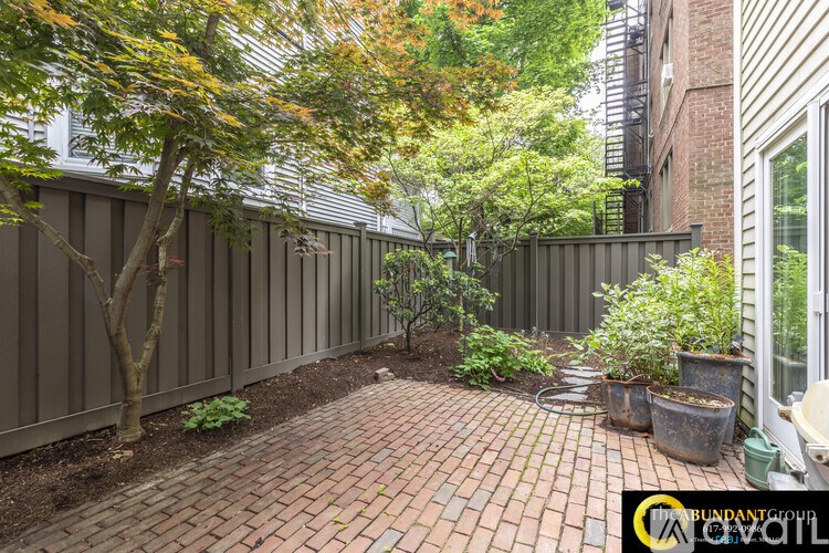 A brick patio is surrounded by a fence and trees.