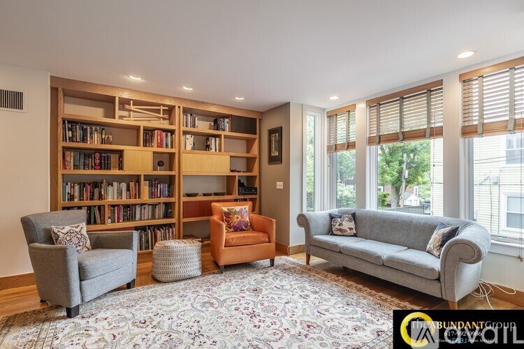 A living room with a grey couch, a chair, a stool, and a bookshelf filled with books.