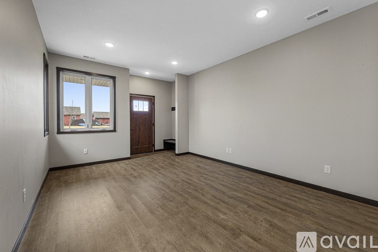 A spacious room with wooden flooring and a window overlooking a residential area.
