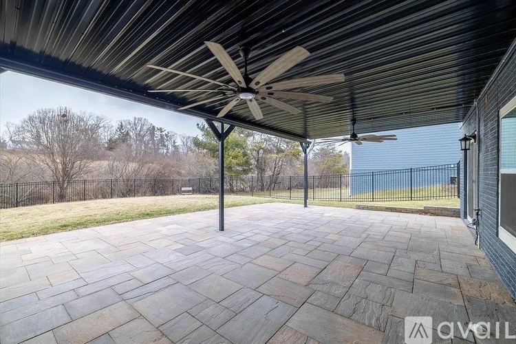 A patio with a fan and a view of a blue fence and trees.