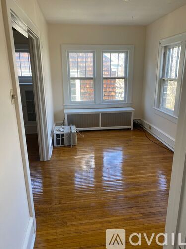 A room with wooden floors and white walls has a window with a view of a building outside.
