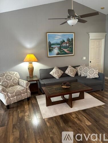 A living room with a grey couch, a patterned armchair, a wooden coffee table, and a painting on the wall.