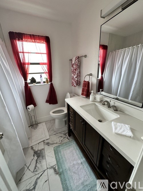 A bathroom with a toilet, sink, and a window with red curtains.