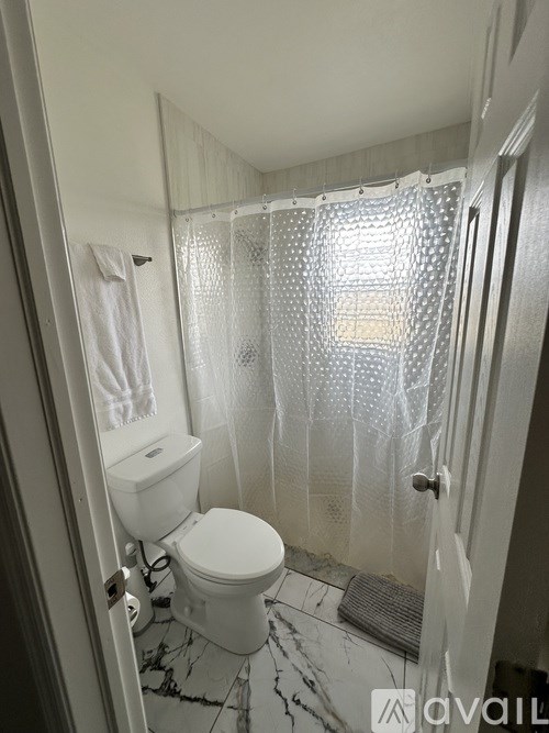 A bathroom with a toilet, a shower curtain, and a mat on the floor.