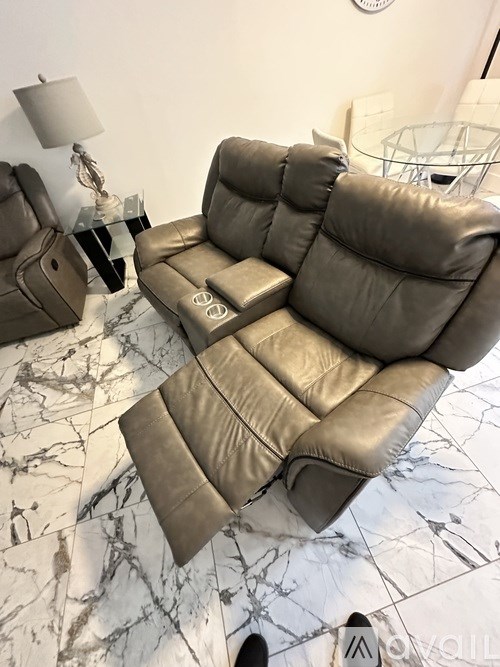 A grey leather reclining sofa with a glass table in front of it.