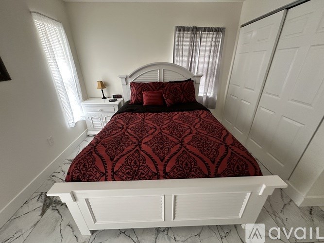 A bed with a red patterned cover sits in a room with white walls and a marble floor.