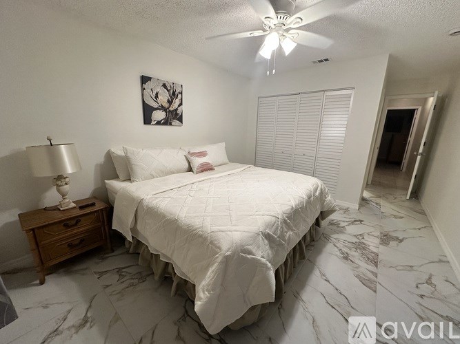 A bedroom with a large bed, a wooden nightstand, and a ceiling fan.