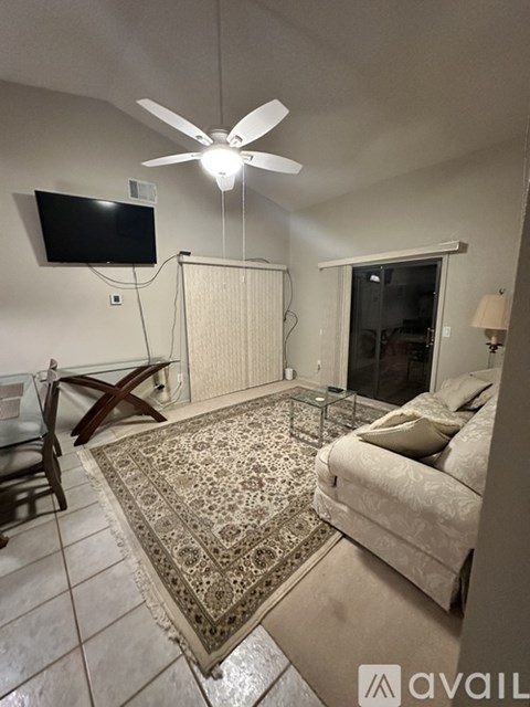 A living room with a rug, a couch, a table, a television and a fan.