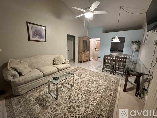 A living room with a white couch, a glass coffee table, and a rug.