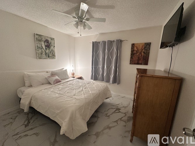 A bedroom with a bed, a TV, and a fan.