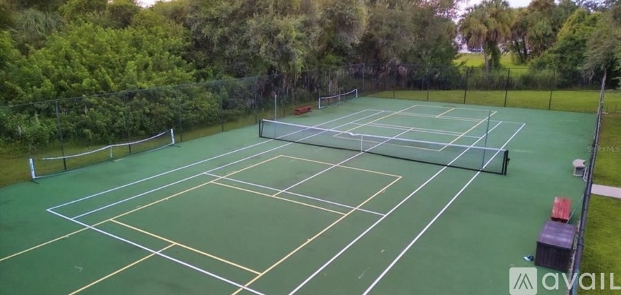A tennis court surrounded by trees and a fence.