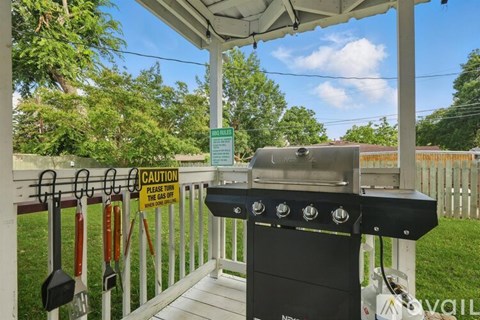 A BBQ grill is on a covered patio with a caution sign attached to the fence.