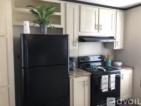 A black refrigerator stands in a kitchen with a stove top oven.