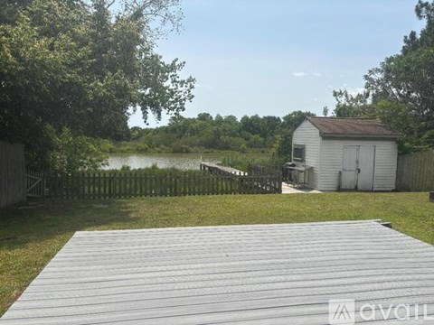 A wooden deck leads to a white shed in a backyard with a fence and a body of water.