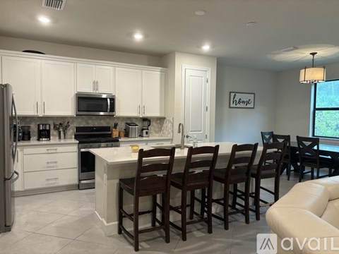 A kitchen with white cabinets and a large island with chairs around it.