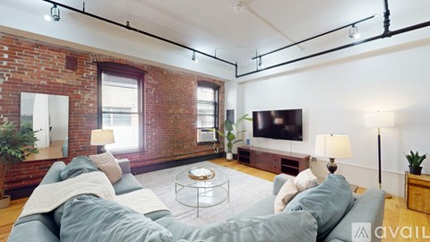 A living room with a grey couch and a brick wall.