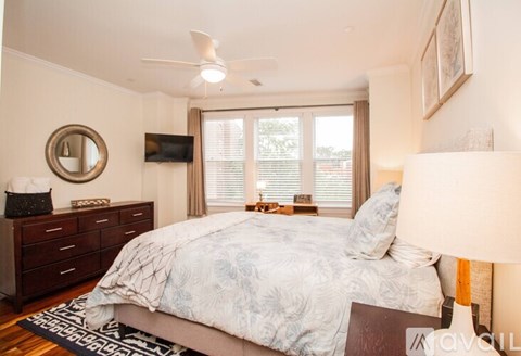 A bedroom with a large bed, a ceiling fan, and a dresser with a mirror.