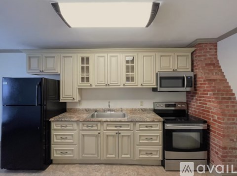 A kitchen with a black refrigerator, a black stove, and a brick wall.