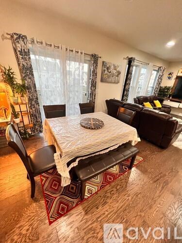 A living room with a brown sofa, a white table with a striped tablecloth, and a red and white patterned rug.