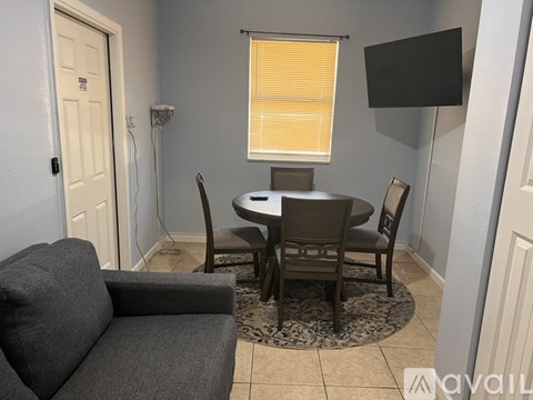 A living room with a grey couch, a round table with four chairs, and a rug.