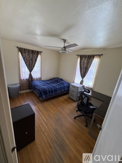 A room with a bed, a desk, and a ceiling fan.