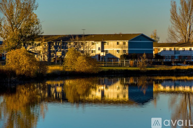 A serene landscape with a building and trees reflected in a calm body of water.