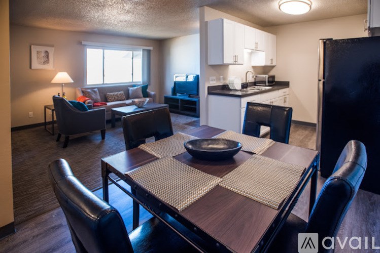 A kitchen area with a table and chairs in the foreground and a living room area with a couch and chairs in the background.