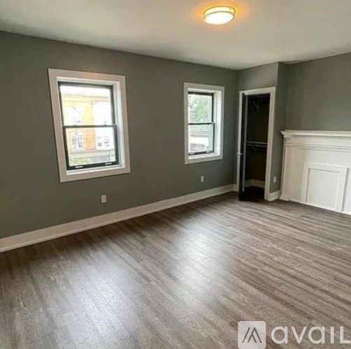 A room with grey walls and wooden flooring, featuring two windows and a door.