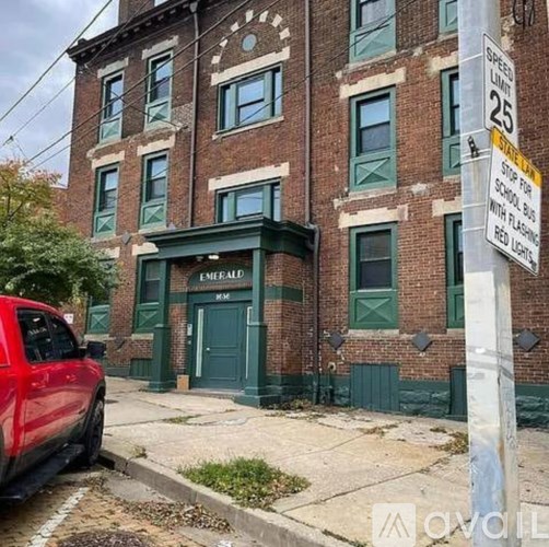 A red car is parked on the side of a street in front of a brick building.