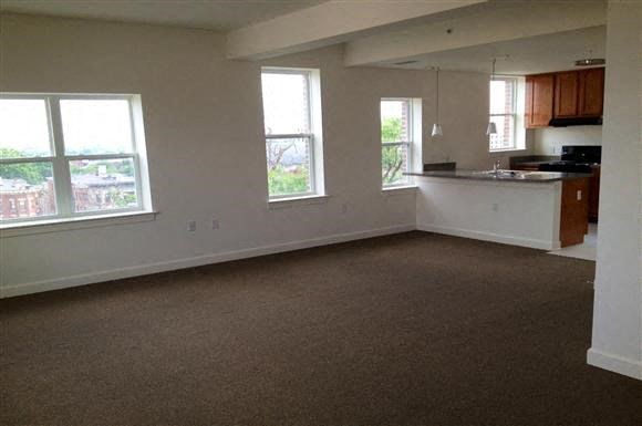 an empty living room with a kitchen and three windows