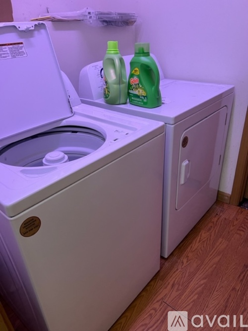 A washing machine with the door open and two bottles of detergent on top of it.