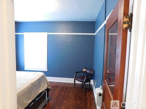 A bedroom with a bed, chair, and blue wall.