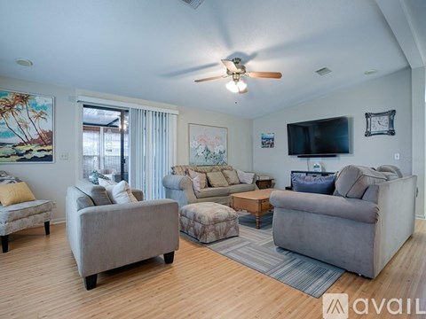 A living room with a grey couch, a brown armchair, a grey chair, a wooden coffee table, a flat screen TV, a ceiling fan, and a painting on the wall.