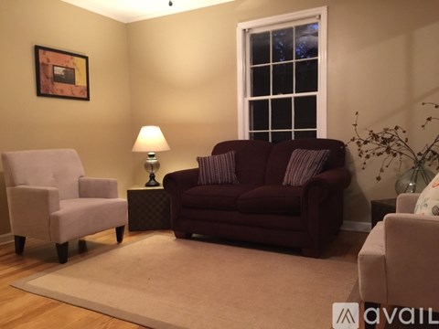 A living room with a red couch, a white chair, and a lamp on a side table.