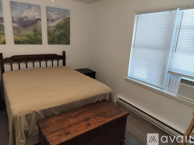 A bedroom with a bed, wooden nightstand, and two mountain paintings on the wall.