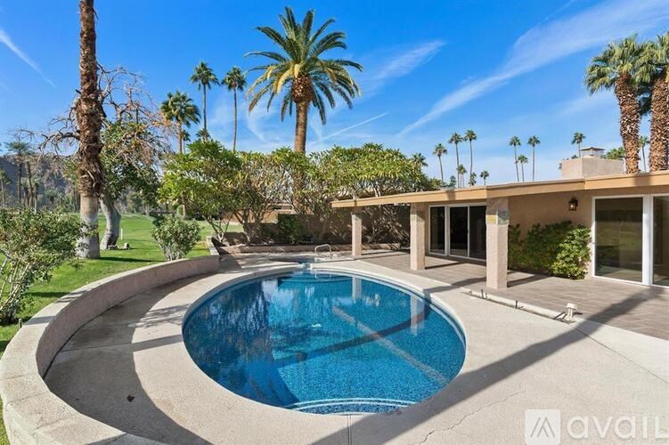 A swimming pool in a backyard with a house and palm trees in the background.