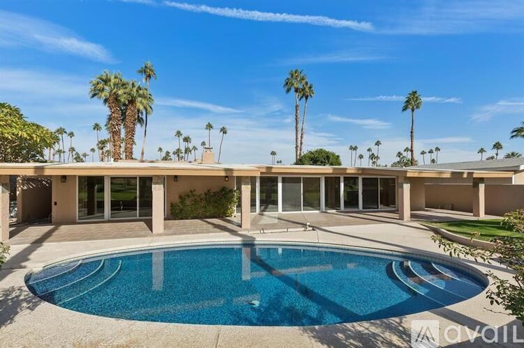 A swimming pool in front of a house with palm trees in the background.