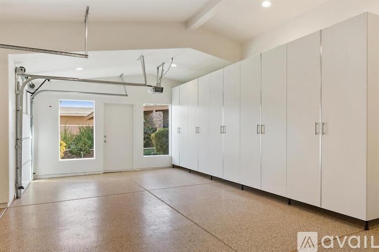 A spacious room with white cabinets and a view of a garden through a glass door.
