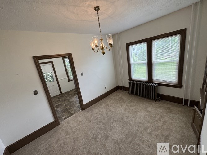 A room with a carpeted floor, a chandelier, and a window with a view of a lawn.
